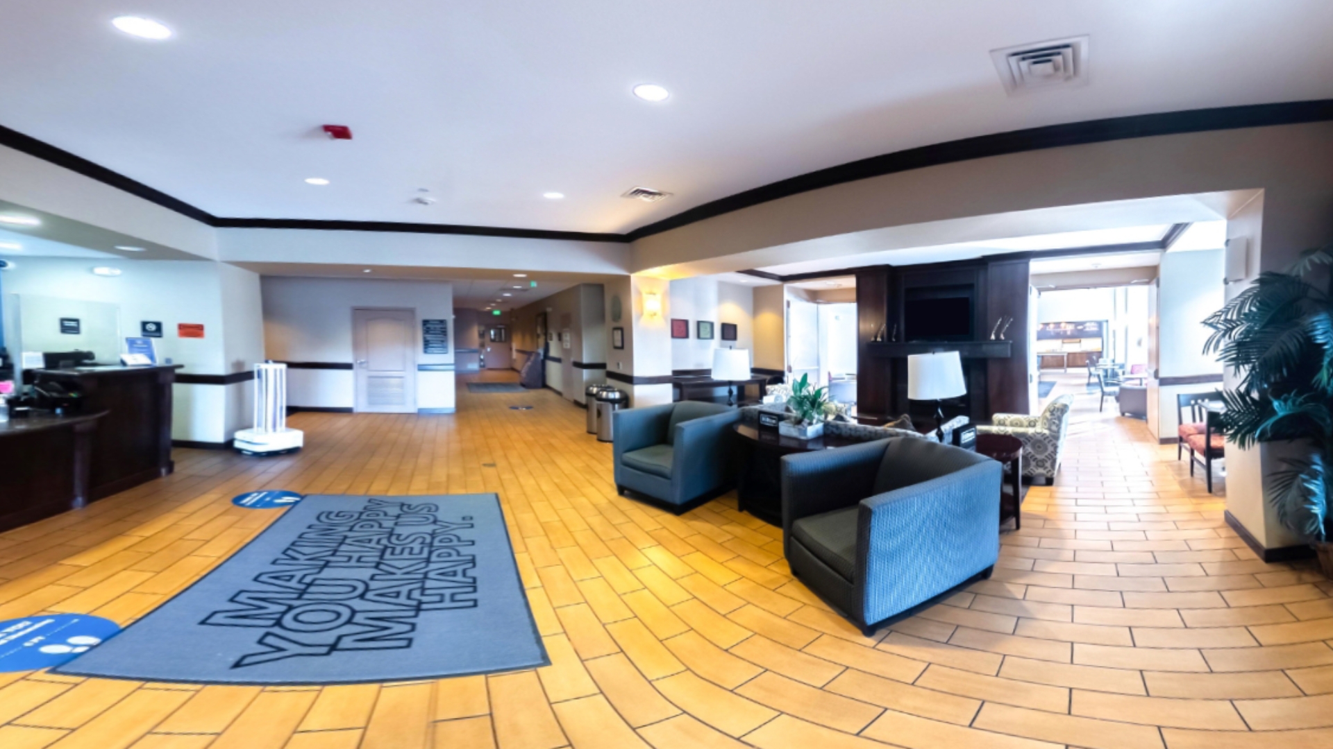 Hotel lobby featuring a spacious area with a large rug, gray couches, and a reception area.